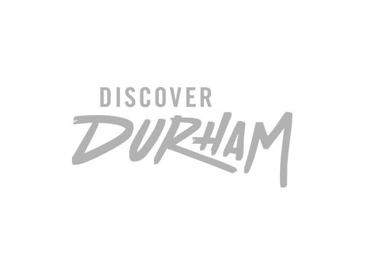 A booklet called Durham Drinks: A Craft Beverage Guide to Durham sits on a table next to a cup of coffee.