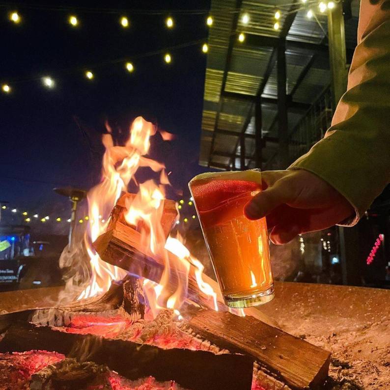 A person holds a beer by firelight at Ponysaurus Brewing Company in Durham, NC.