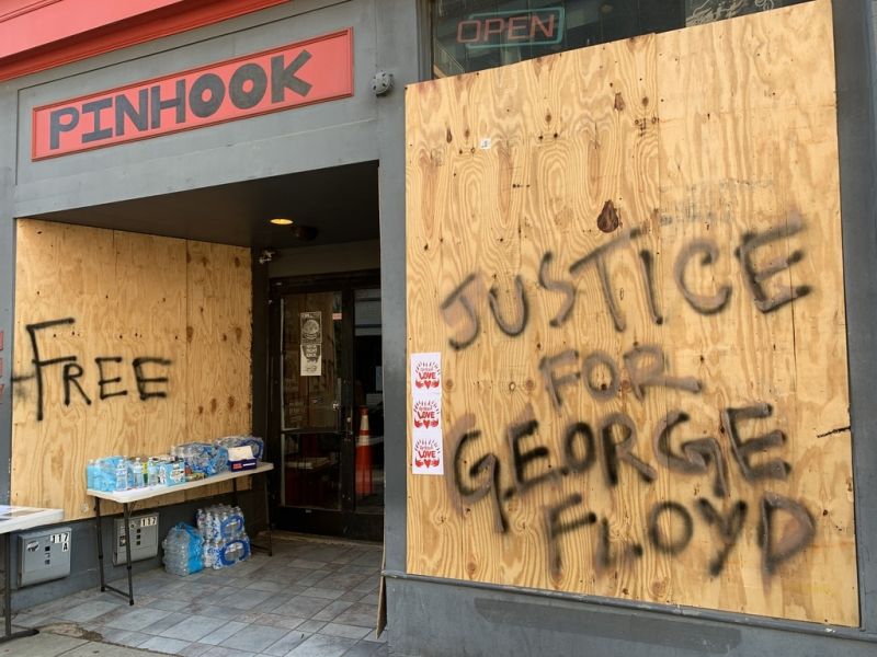 The windows of The Pinhook are boarded up with "justice for George Floyd" spray painted on the boards.