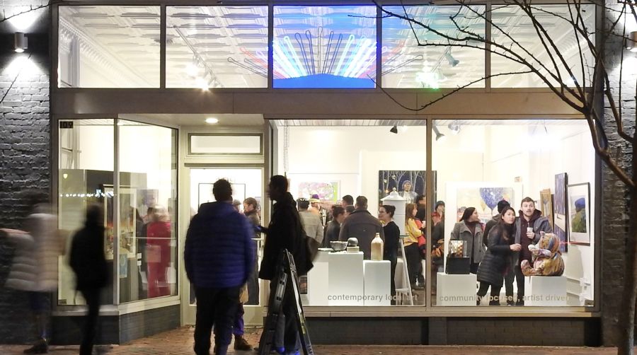 A nighttime view of a crowd inside a 5 Points Gallery from the outside.