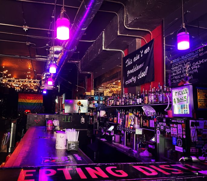 Purple lights wash over the bar at The Pinhook with a Pride flag in the background.