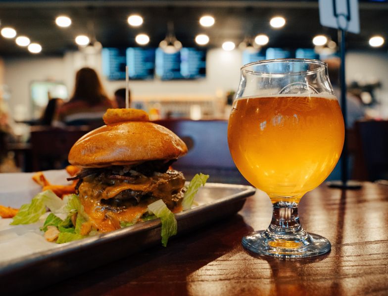 Cheese melts over a crispy burger next to a bubbling beer from Tobacco Wood Brewing.