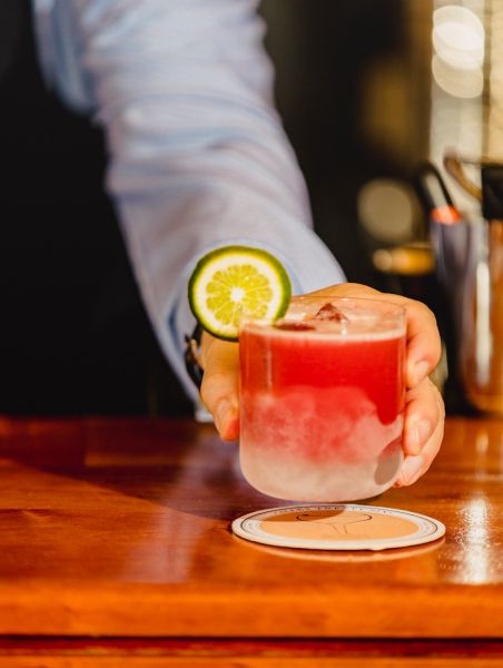 A hand clutches the pink and white Mexican Herbalist, a cocktail from Alley Twenty Six.