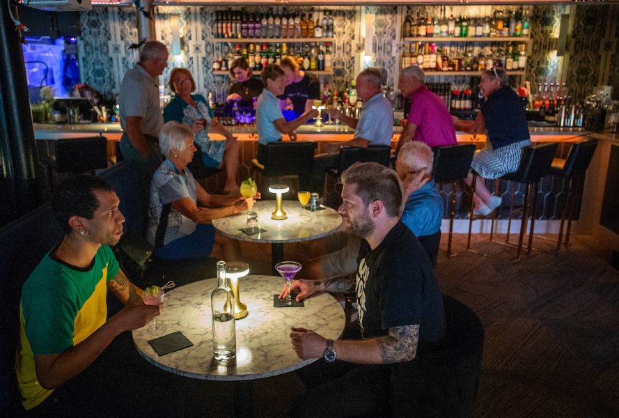 A crowd of adults of all ages sit and enjoy cocktails at tables and at the bar at Corpse Reviver.