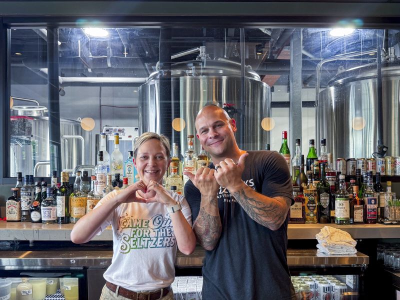 The owners of Fizzwerks stand in front of their brewery with their hands showing the Love Durham signs.