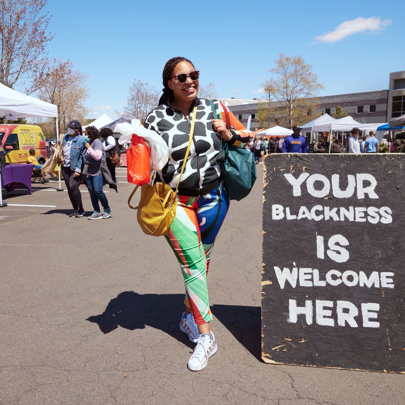 A woman smiles next to a sign at The Black Farmers Market in Durham, NC.