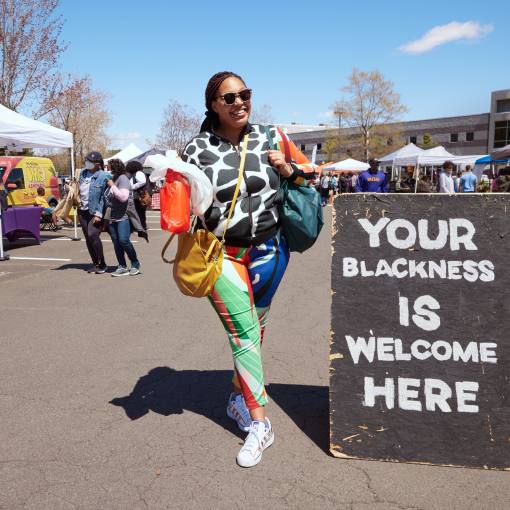 A woman smiles next to a sign at The Black Farmers Market in Durham, NC.