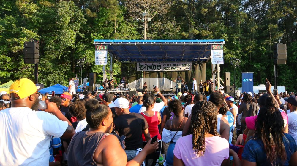 Many Bimbé festival goers gather in front of a stage enjoying live music.