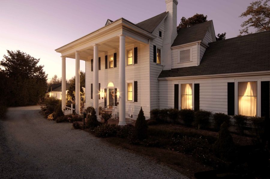 The exterior of Arrowhead Inn at sunset. A white, two-story colonial home with four columns on the front porch.