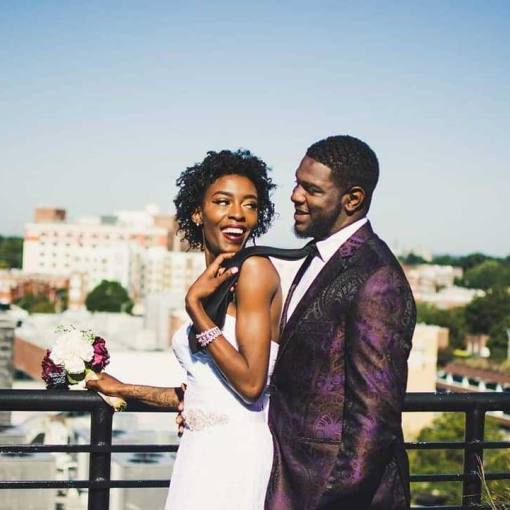 A newlywed couple stand on a balcony overlooking Downtown Durham