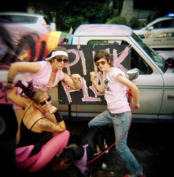 Three individuals in pink stand next to a truck with signs on it.