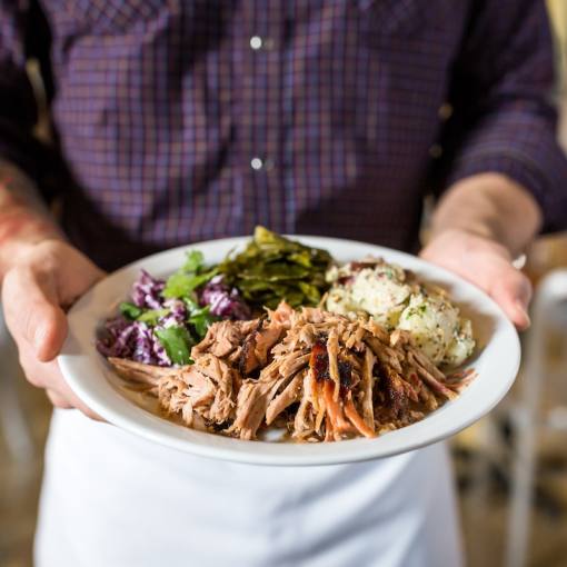 A person in an apron holds a plate of delicious Barbecue from Picnic up close so the camera can get all the details.