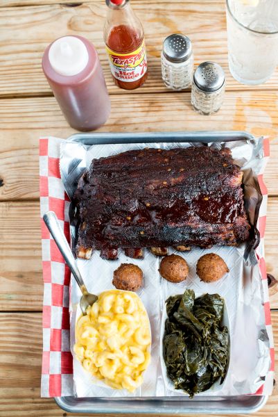 A plate of ribs, collards, hush puppies, and mac n' cheese from the Blue Note Grill sits on a picnic table looking tasty.