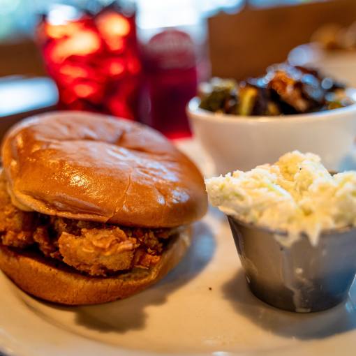 A fried chicken sandwish lays on a plate next to a side and coleslaw.