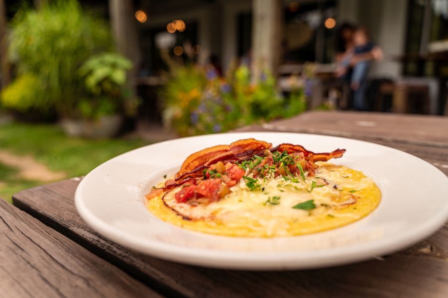 A bacon and grits bowl from Foster's Market in Durham foregrounds the storefront.