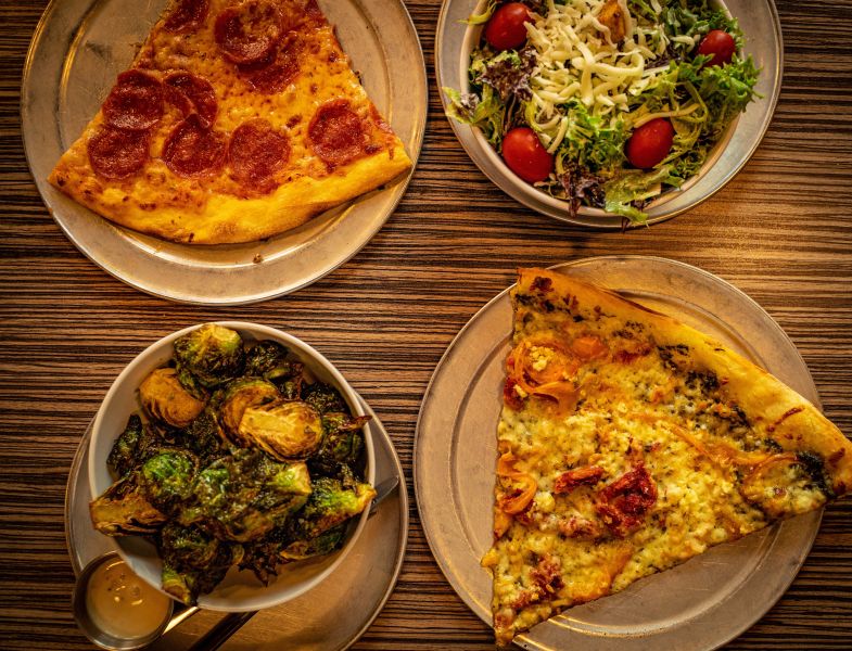 Two slices of pizza sit diagonal from each other next to a side of brussels sprouts and caesar salad.