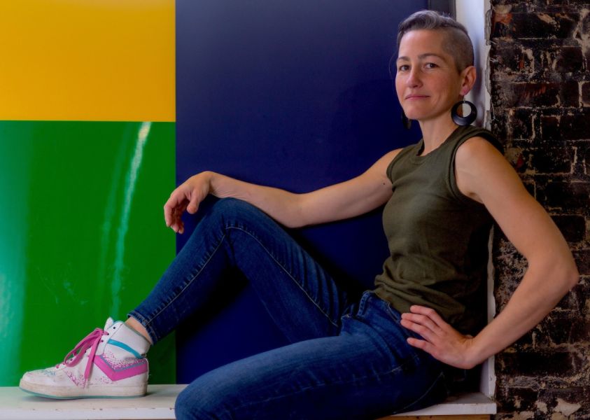 A woman sits in a windowsill in front of a colorful, geometric print of green and blue.