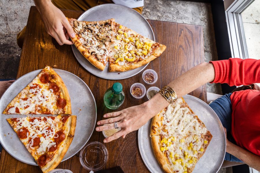 Friends hover over large pizza slices at Sofia's Pizza in East Durham.