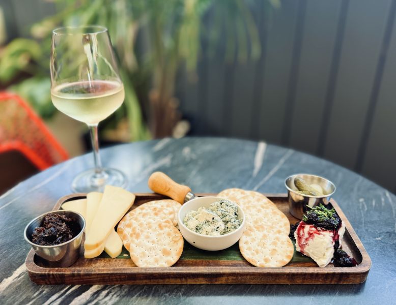 A cheese and cracker plate sits on a table next to a glass of white wine at The Velvet Hippo.