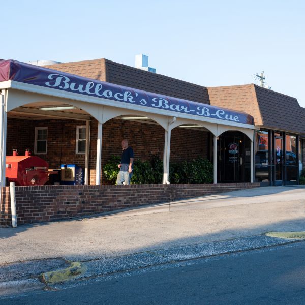 White pillars hold up the red roof of Bullock's Barbecue as an employee watches over the smoker under the overhang.