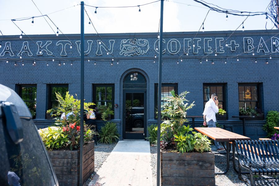 The front facade of Aaktun Coffee & Bar in Durham, a grey brick building with tables outside.