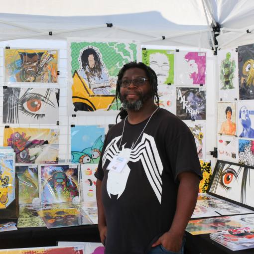 An artist stands in front of paintings for sale at Centerfest in Durham, NC.