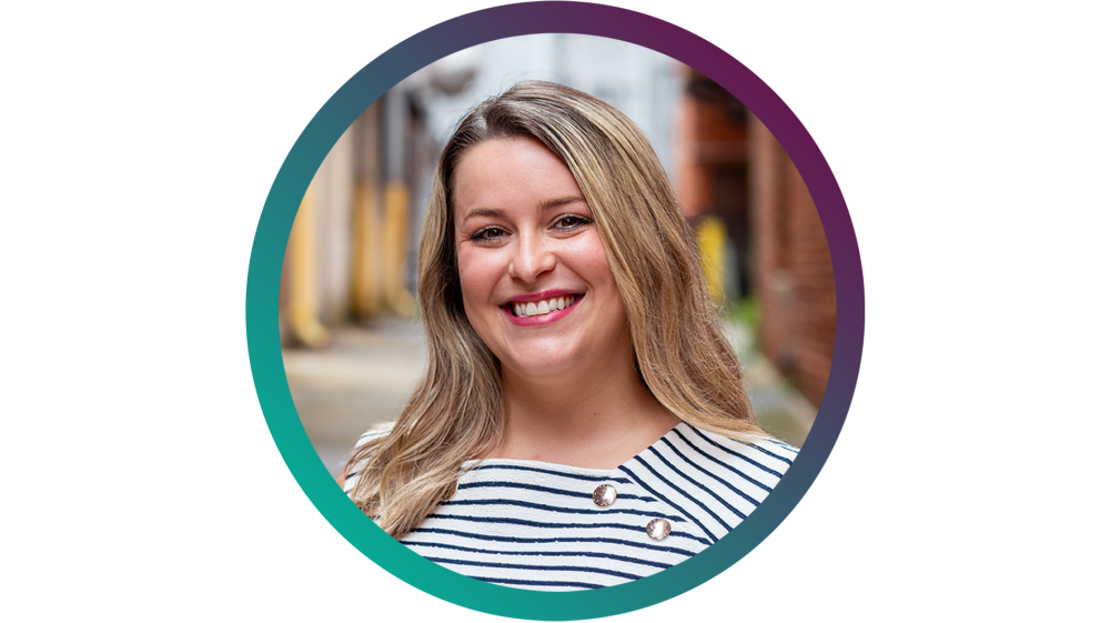 A blonde woman wearing a blue and white striped shirt smiles at the camera.