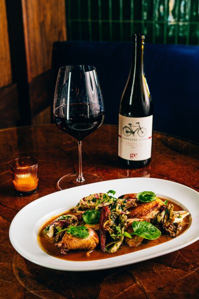 A glass of red wine sits full next to its bottle overlooking a chicken dish at Nana's in Durham.