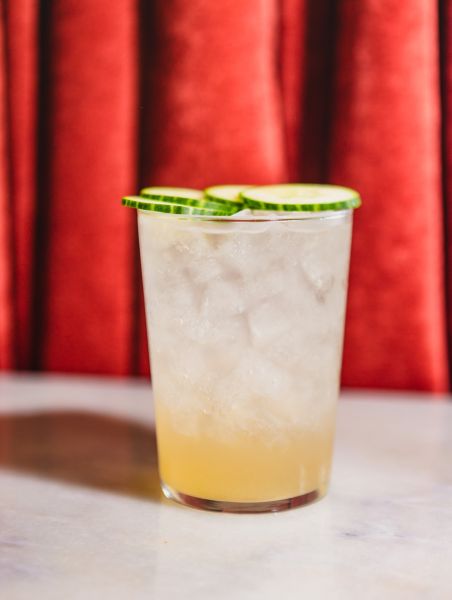 A cocktail from Mateo Bar de Tapas sits in front of a red curtain.