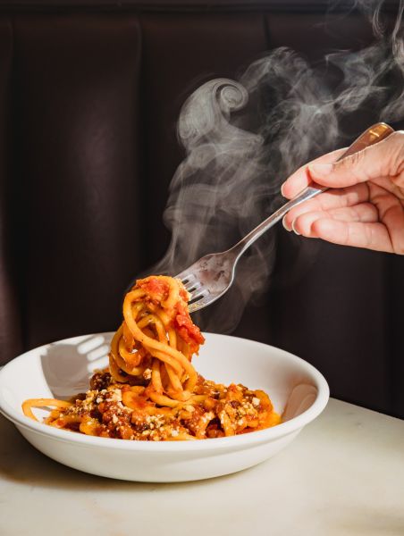 A hand twirls a fork into a steaming bowl of bucatini from Mothers & Sons in Durham