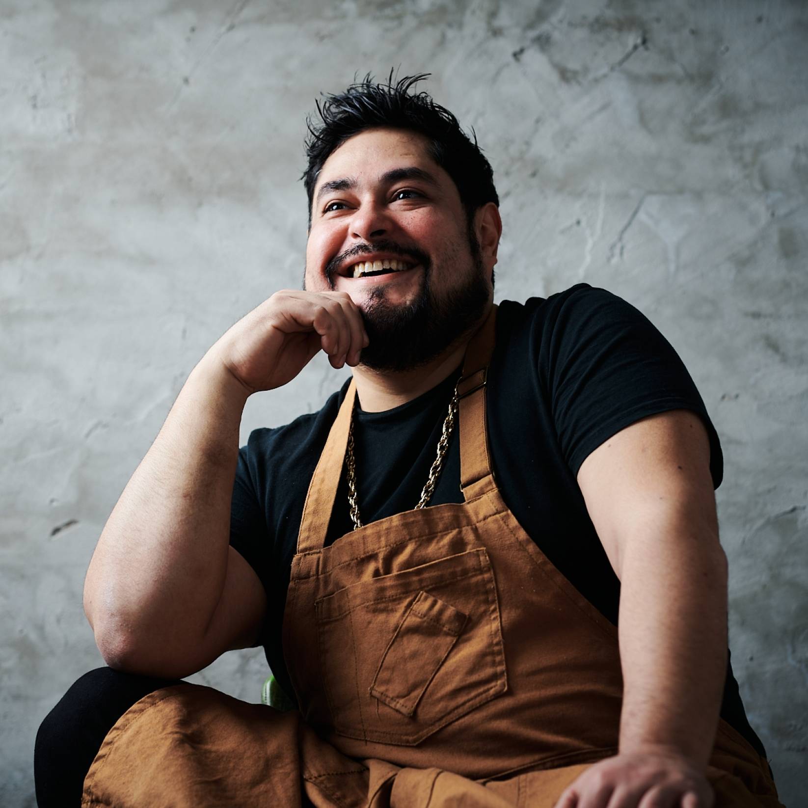 Chef Oscar Diaz smiles for the camera in front of a grey back drop.