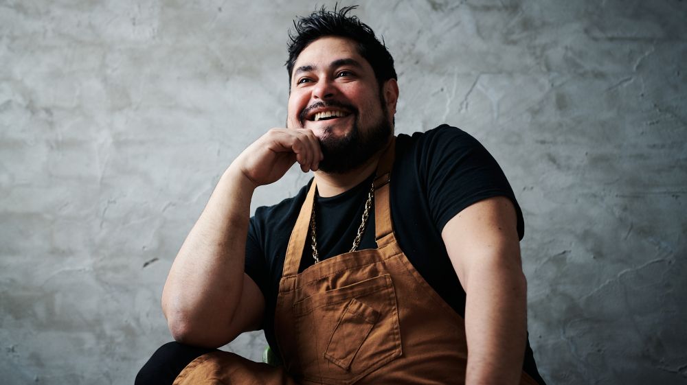 Chef Oscar Diaz smiles for the camera in front of a grey back drop.