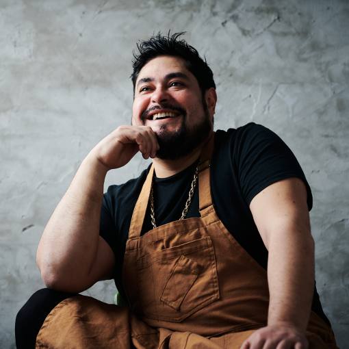 Chef Oscar Diaz smiles for the camera in front of a grey back drop.