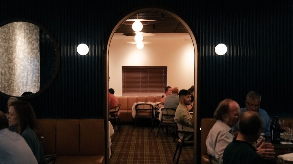 A view from one dining room through an arched doorway into another room where tables are full of diners.