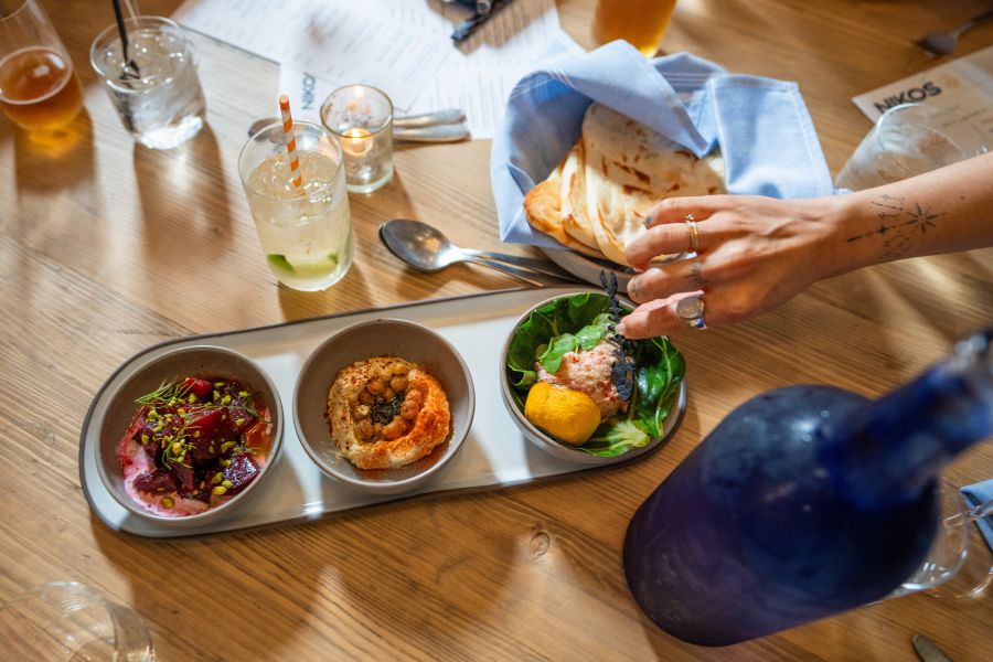 A hand reaches for a green meze spread at Nikos in Durham, NC.