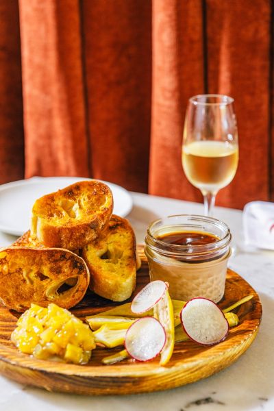 Toasted garlic bread sit on a plate with salsa and spreads in front of a glass of white wine at Mateo.