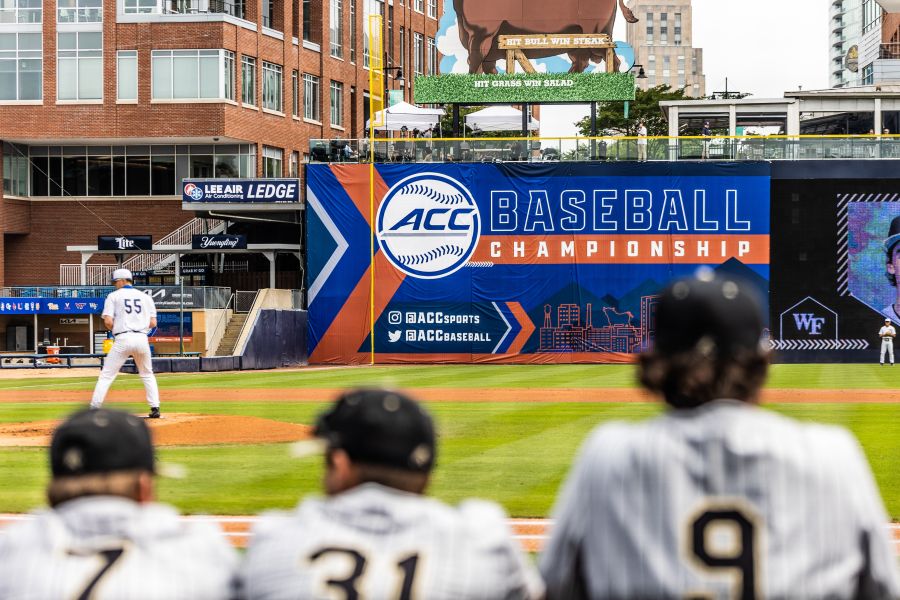 Three college baseball players lean on the railing in front of the ACC Baseball Championship sign at DBAP.