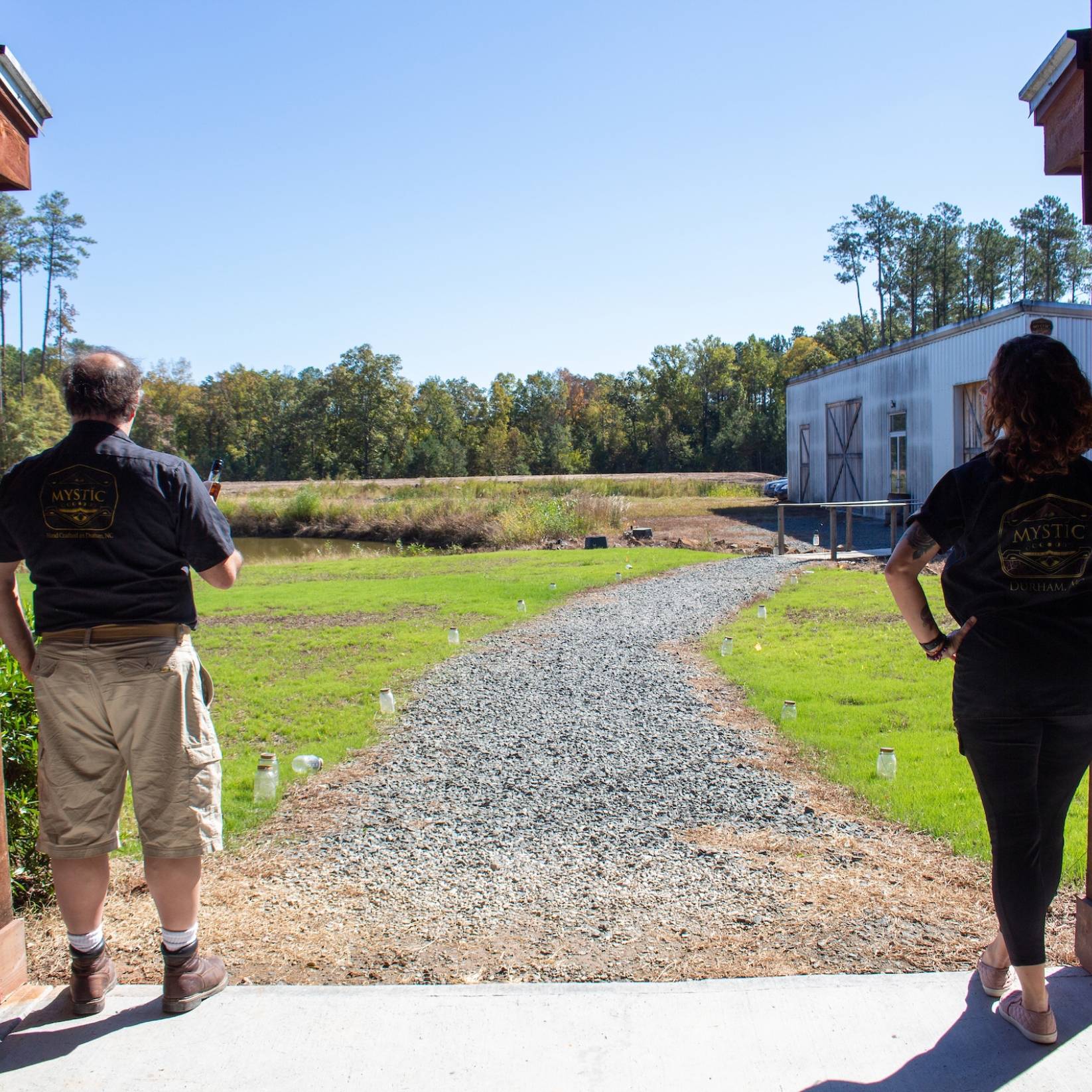 Two employees of Mystic Farm &amp; Distillery stand with their backs to the door, looking out onto the farm.
