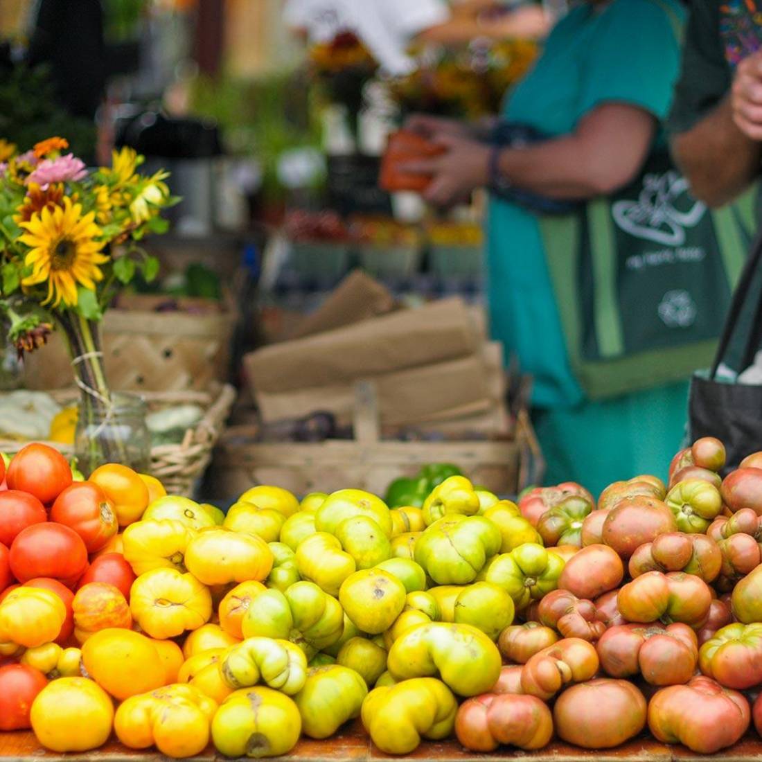 At the Durham Farmers Market, a customer stands behind a table full of tomatoes of different colors.