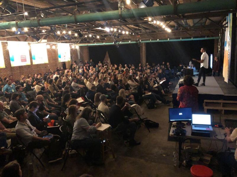A person performs on a stage in front of a crowd of people in a brick-lined space at The Fruit.
