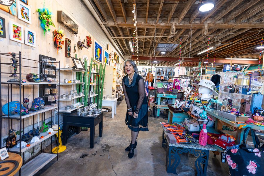 The owner of Cecy's Gallery stands, laughing, between the art and jewelry in the store.