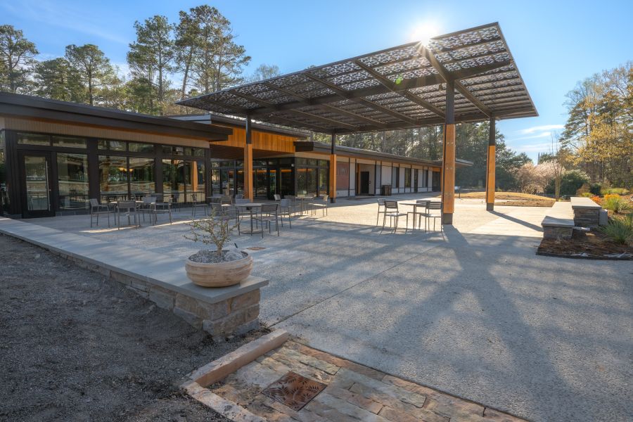 A visitor center to the right has a roof that shades an outdoor seating area. In the distance, cherry blossoms bloom.