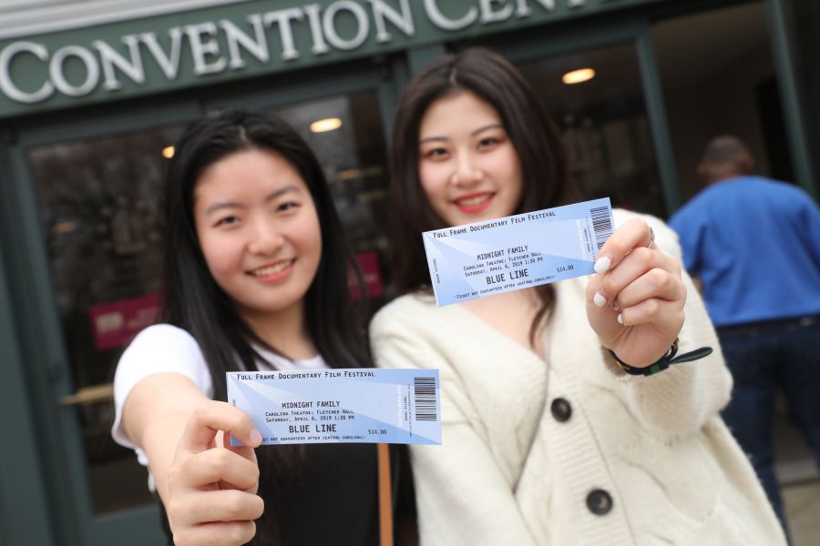 Two women hold movie tickets up to the camera in front of the Durham Convention Center.