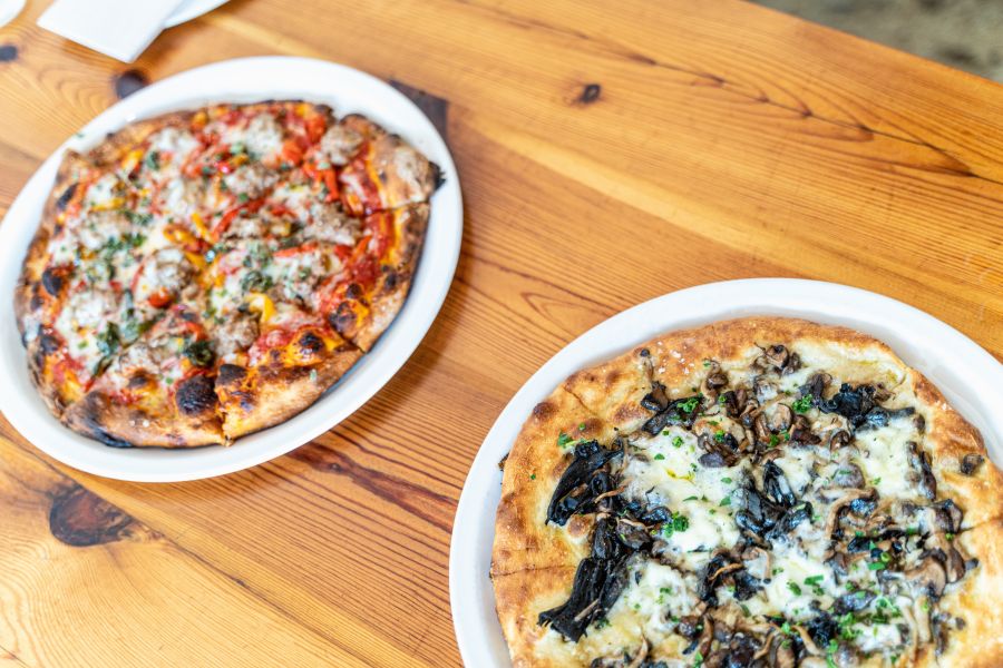 Two specialty pizzas from Pizzeria Toro sit on a table with steaming, fluffy crusts.