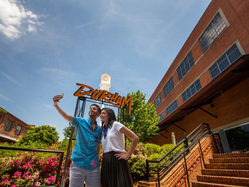 A couple poses for a selfie in front of the Durham sign at American Tobacco Campus.