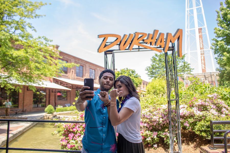 A couple takes a selfie in front of the iconic iron Durham sign.