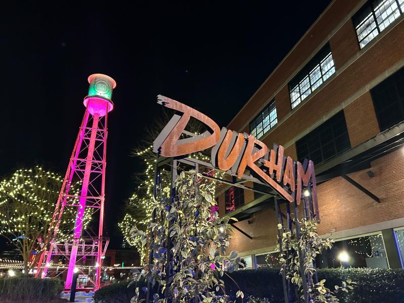 Lucky Strike water tower lit from below with magenta lights in the background; foreground is a Durham sign.