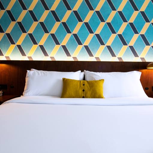 In front of a blue geometric wall design, a freshly made bed awaits guests at Unscripted Hotel in Durham