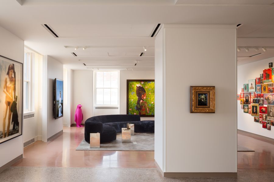 An art gallery with artwork on each wall and a column in the center of the room. A sofa sits on the floor in the middle.