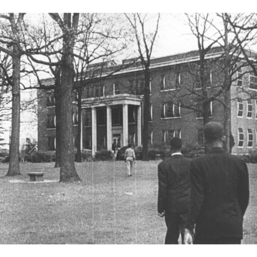 A black and white photo depicts two individuals standing in front of the historic Lincoln Hospital in Durham.